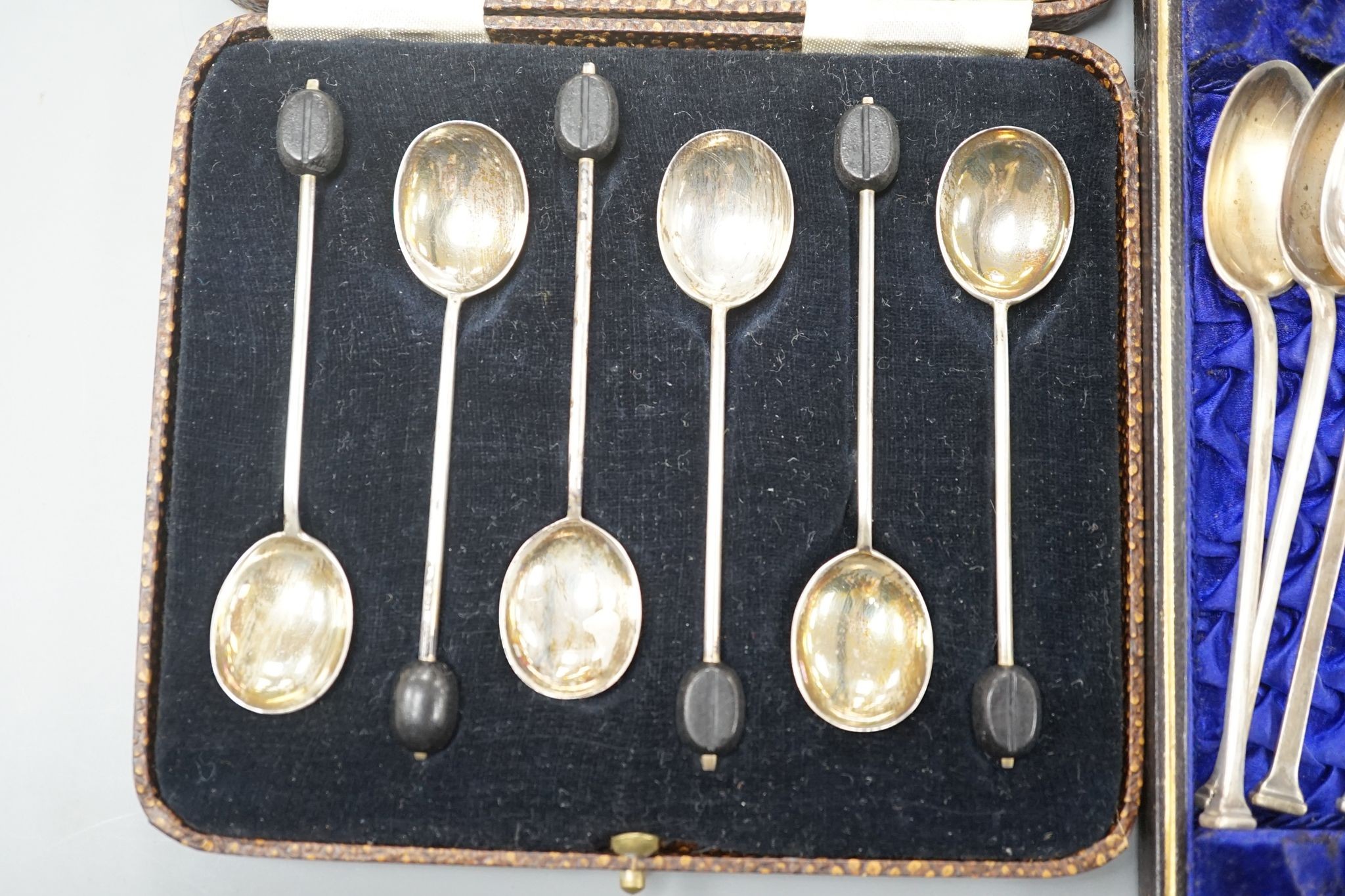 A cased set of six silver bean end coffee spoons, two other sets of six teaspoons and a pair of silver sugar tongs.